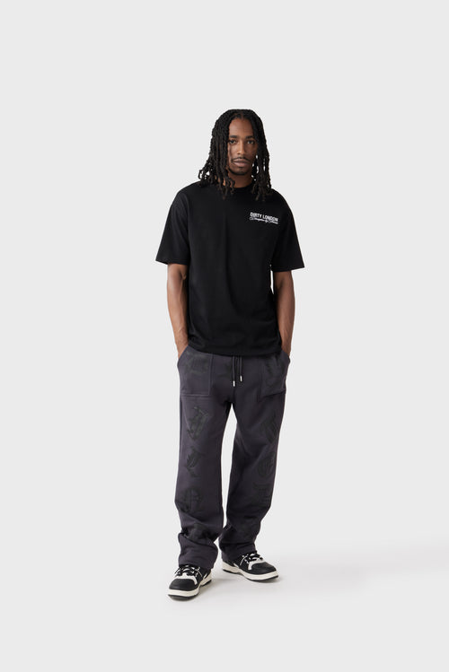 Model wears a black oversized T‑shirt with a white 'Dirty London' logo and the cursive phrase 'Disruptive by Nature' on the left chest. The relaxed fit and ribbed crew neck give a casual look.