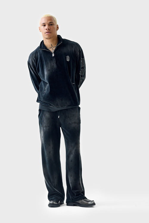 Full‑body view of model wearing black acid‑wash straight track pants with matching jacket; pants feature drawstring waistband, rhinestone 'DL' patch pocket, wide‑leg cut and acid‑wash texture.