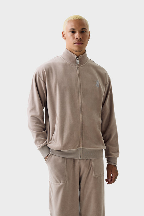 Model wearing Fungi‑coloured velour zip‑through track jacket and matching pants; jacket has high collar, full zip, diamanté ''DL'' monogram on chest, ribbed cuffs and hem, and side pockets.