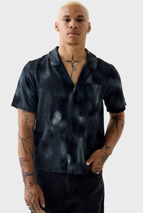 Front view of the black acid‑wash short‑sleeve shirt on a model showing open collar, chest pocket and washed pattern.