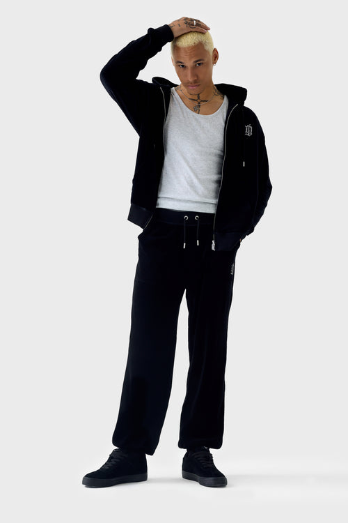 Full‑body front view of model wearing a black zip‑through hoodie unzipped over a grey T‑shirt with matching pants; features hood, rhinestone 'DL' monogram on chest, kangaroo pockets, ribbed cuffs and hem.