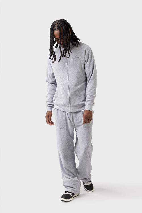 Model pairing the grey velour track pants with a grey crew-neck sweatshirt. The diamante 'Dirty London' logo near the pocket and the drawstring waistband stand out against the marl texture, offering an alternative styling option.