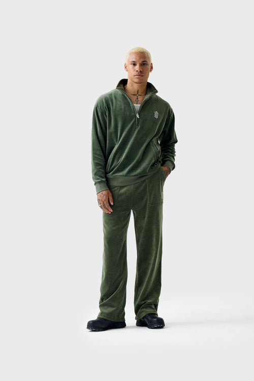 Full‑body view of the thyme‑green velour half‑zip track top zipped halfway. The top has a high collar, diamanté 'DL' logo on the chest, ribbed cuffs and hem, and is worn with matching pants.