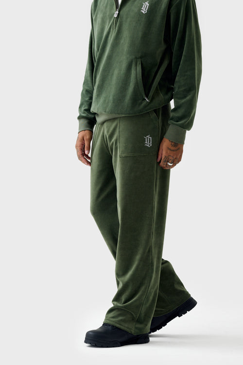 Front view of model wearing green velour straight track pants with matching jacket zipped up; pants have drawstring waist, rhinestone 'DL' patch pocket and wide-leg silhouette.