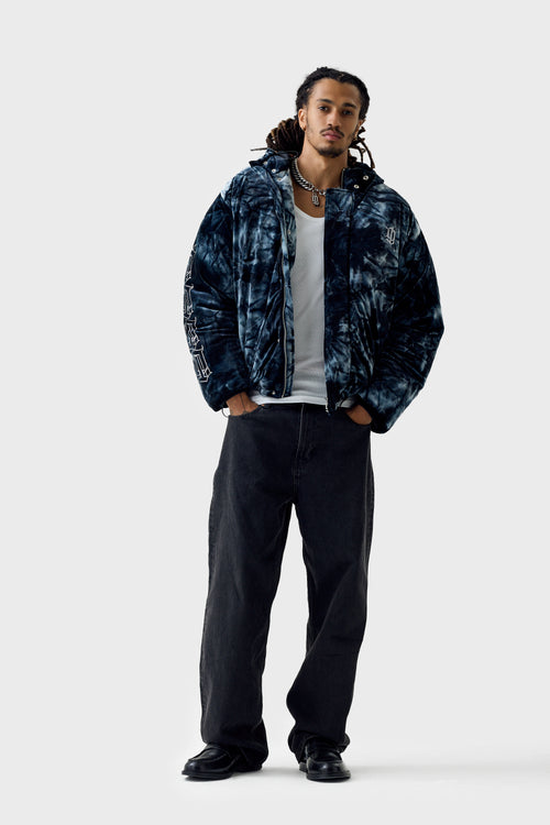 Full‑body front view of a model wearing the blue acid tie‑dye puffer jacket zipped up with high collar and ''DL'' monogram on chest, showing swirling tie‑dye pattern and cropped length.