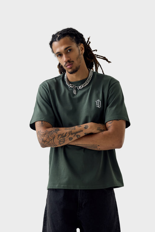 Front view of model wearing thyme green T-shirt with small white 'DL' monogram on left chest, ribbed crew neck and relaxed fit.