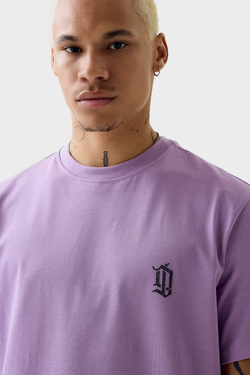 Front close-up of purple short-sleeve T-shirt showing small black rhinestone 'DL' monogram on left chest, ribbed crew neck and solid colour.