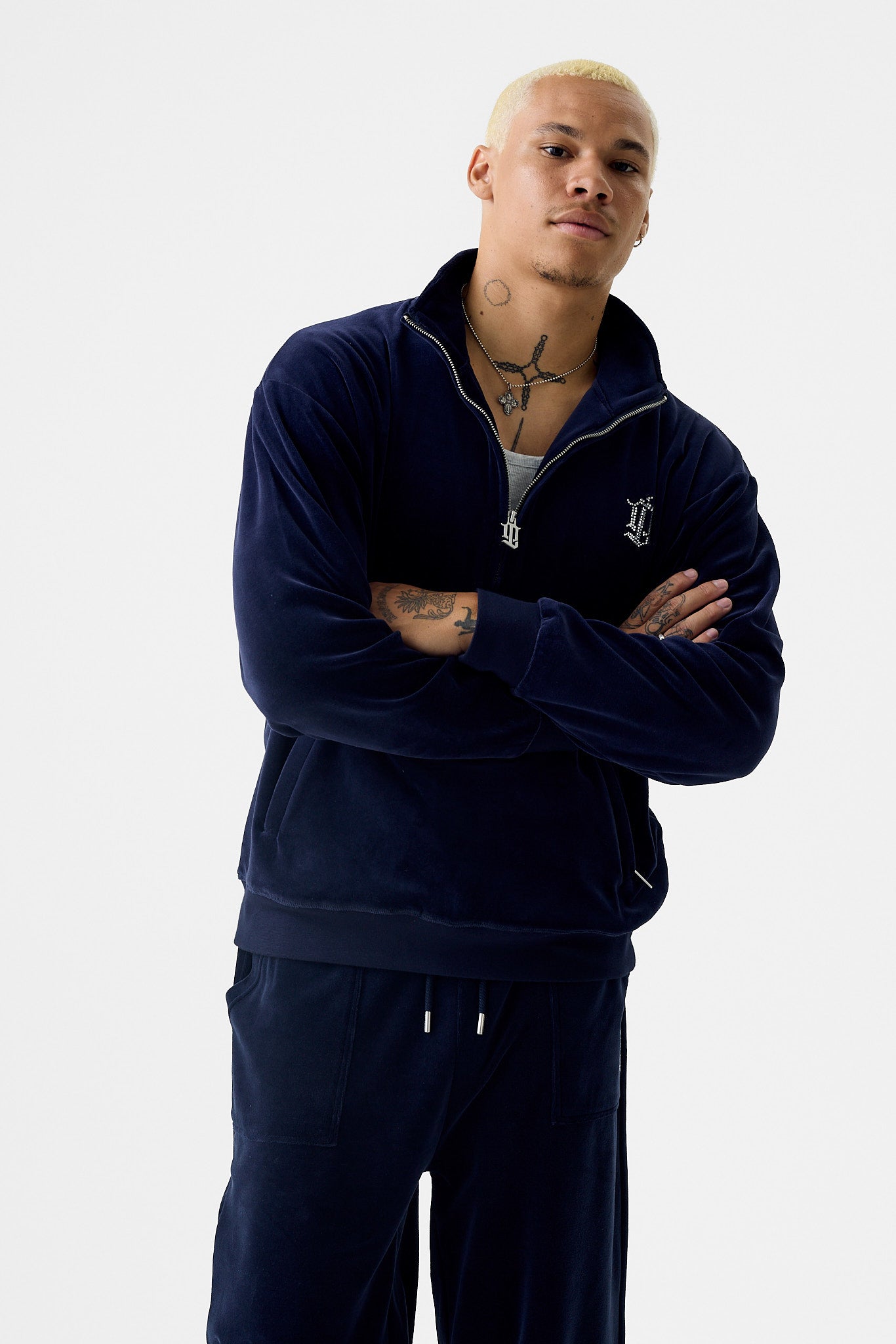 Full-body view of the navy cotton half‑zip track jacket zipped up to a high collar. The jacket features a diamanté 'DL' monogram on the left chest, ribbed cuffs and hem, and side pockets. The matching pants and cotton texture give a relaxed fit.